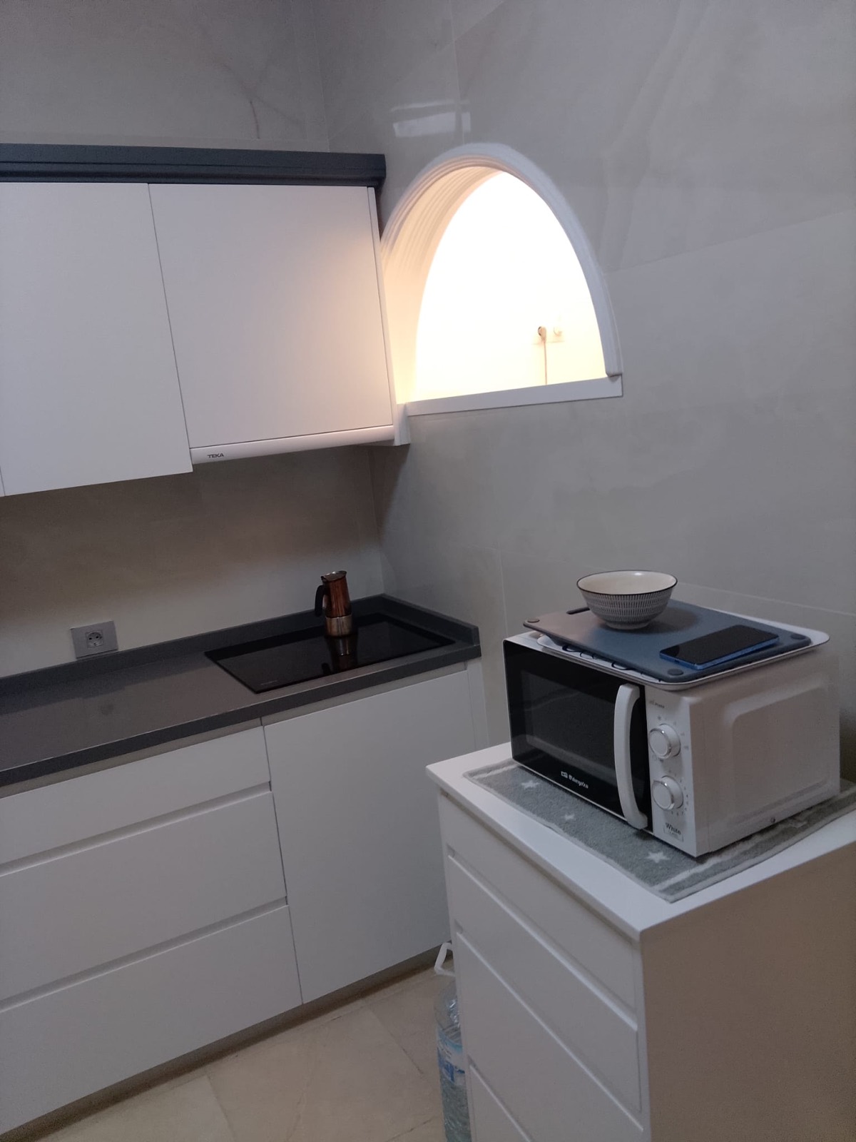 Cocina en L reformada con muebles blancos y ventana en arco